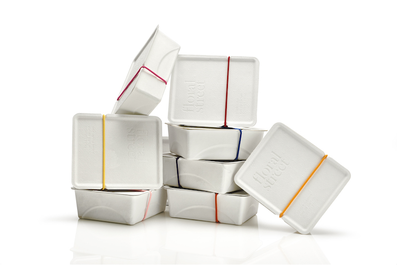 Stack of minimalist white “Floral Street” boxes secured with colorful elastic bands, arranged against a clean white background.