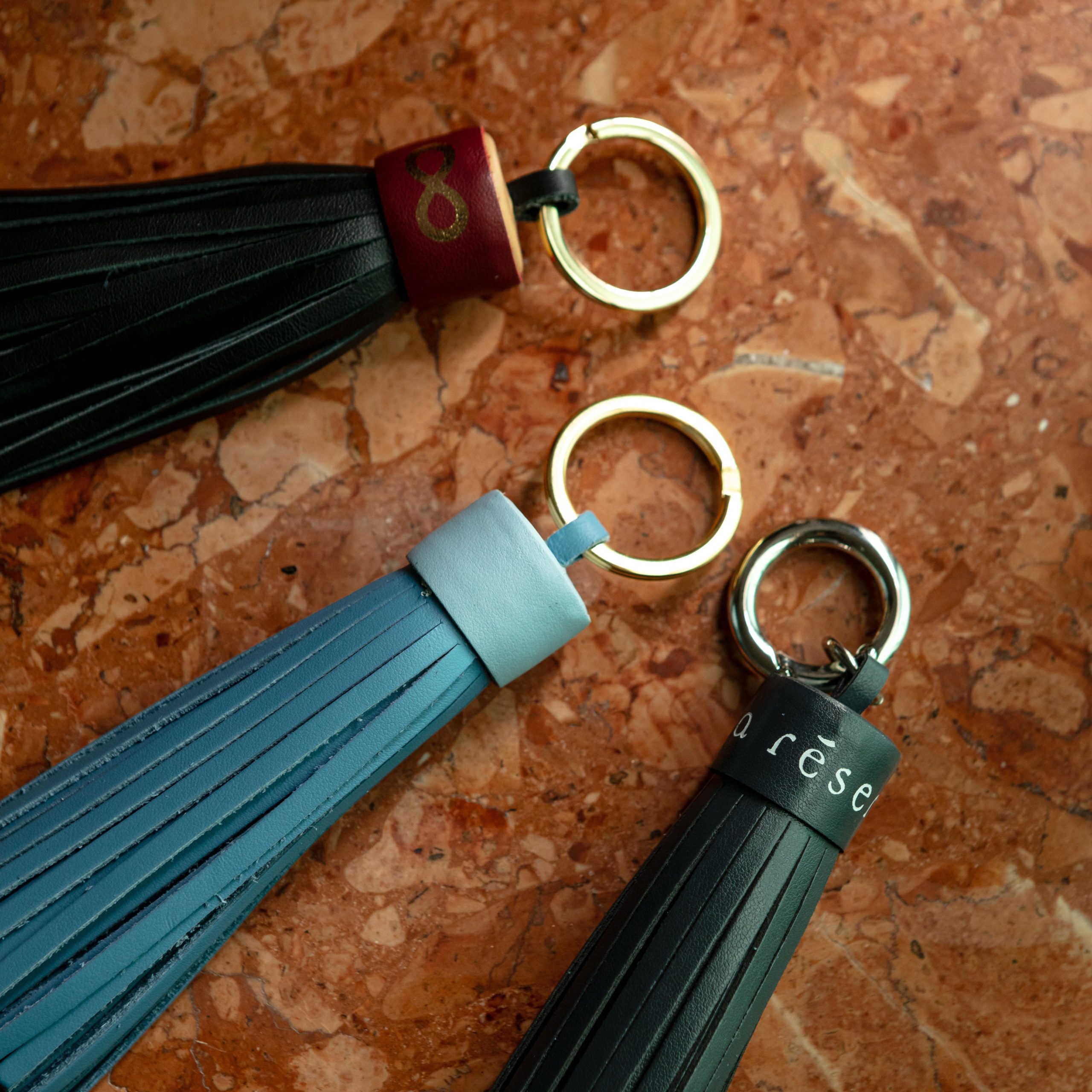 Leather tassel keychains with metal rings displayed on a marble surface.