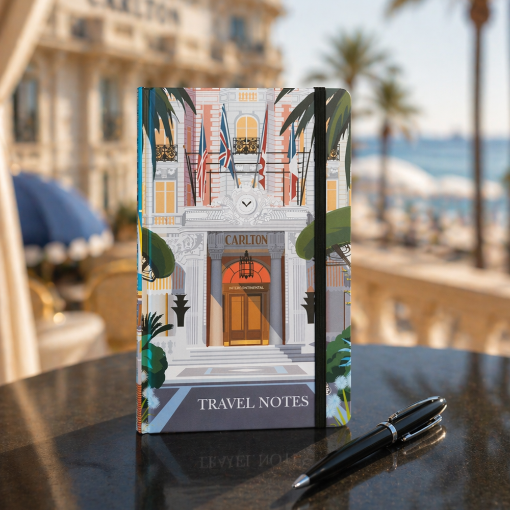 Illustrated travel notebook and pen displayed on an outdoor table with a seaside hotel backdrop.