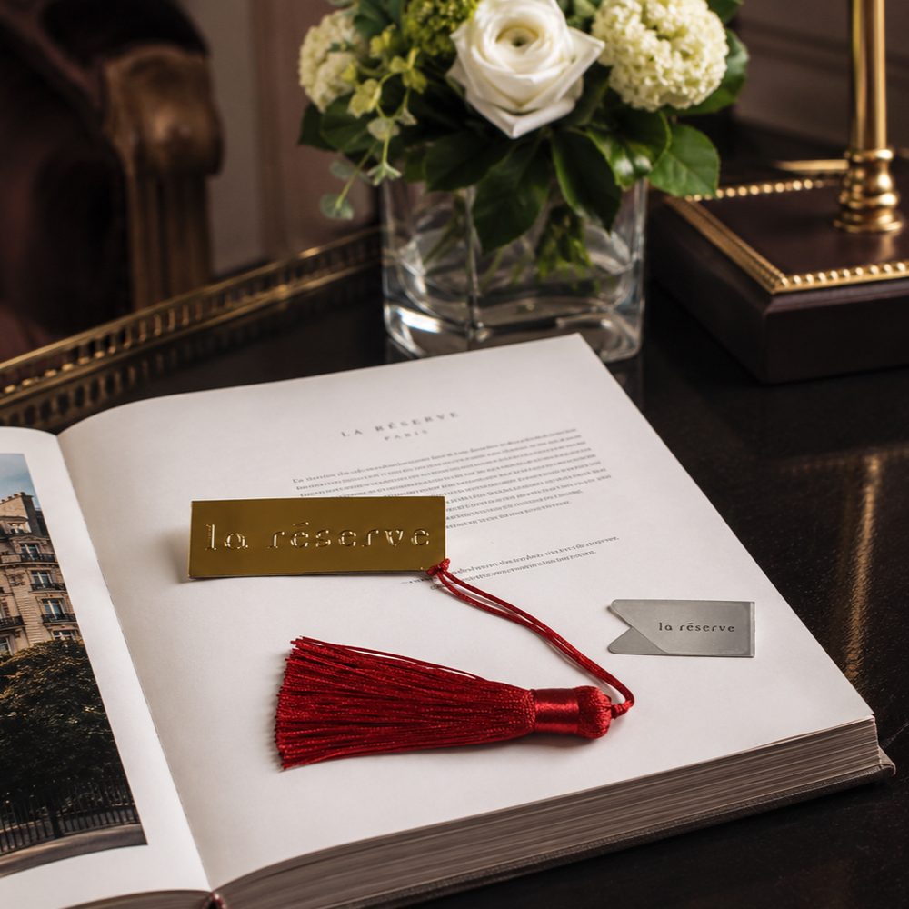 Metal bookmark and paper clip with a red tassel resting on an open book.