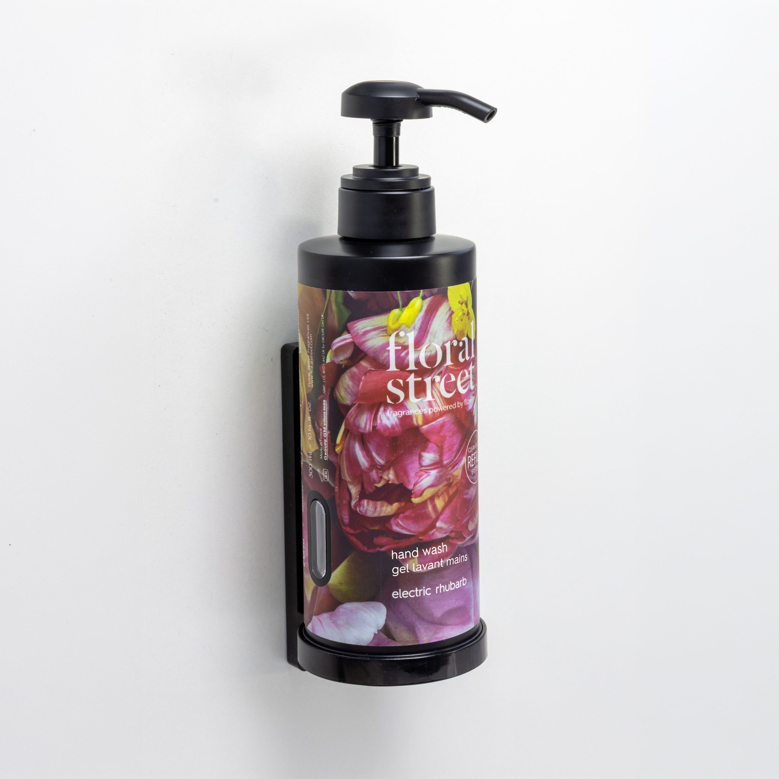 Floral Street Electric Rhubarb hand wash in a refillable wall-mounted dispenser with black pump, minimalist white wall background.