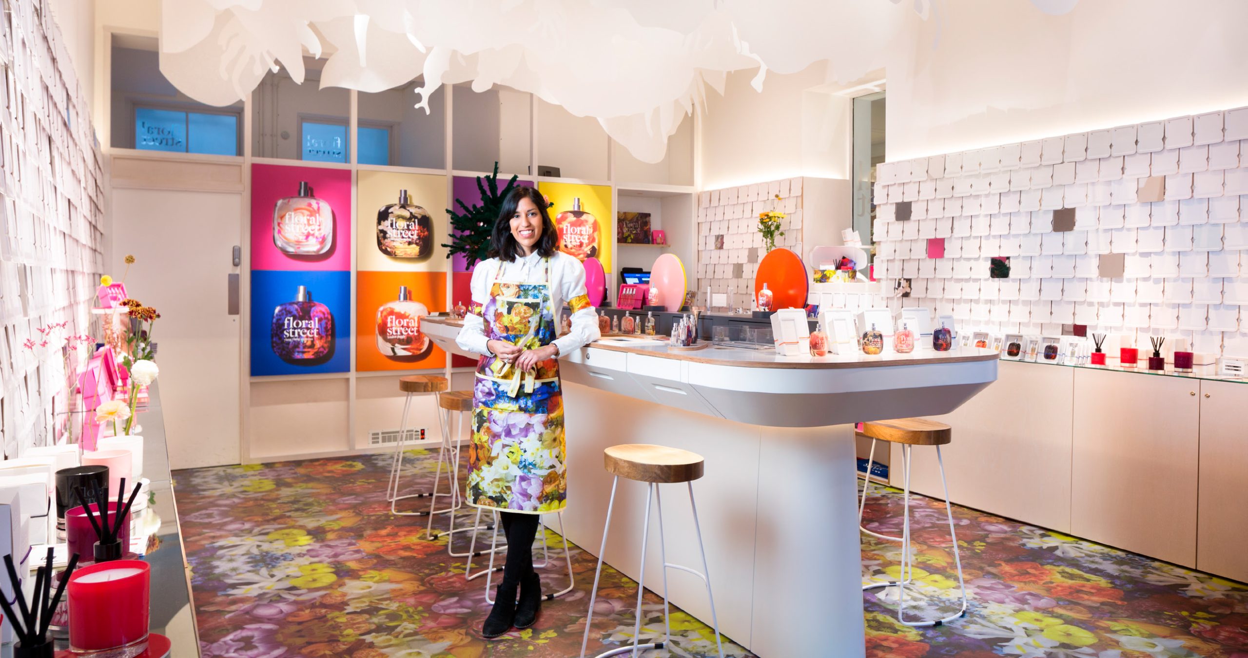 Colorful perfume shop interior with a person behind a counter, surrounded by “Floral Street” fragrance displays and bright decor.