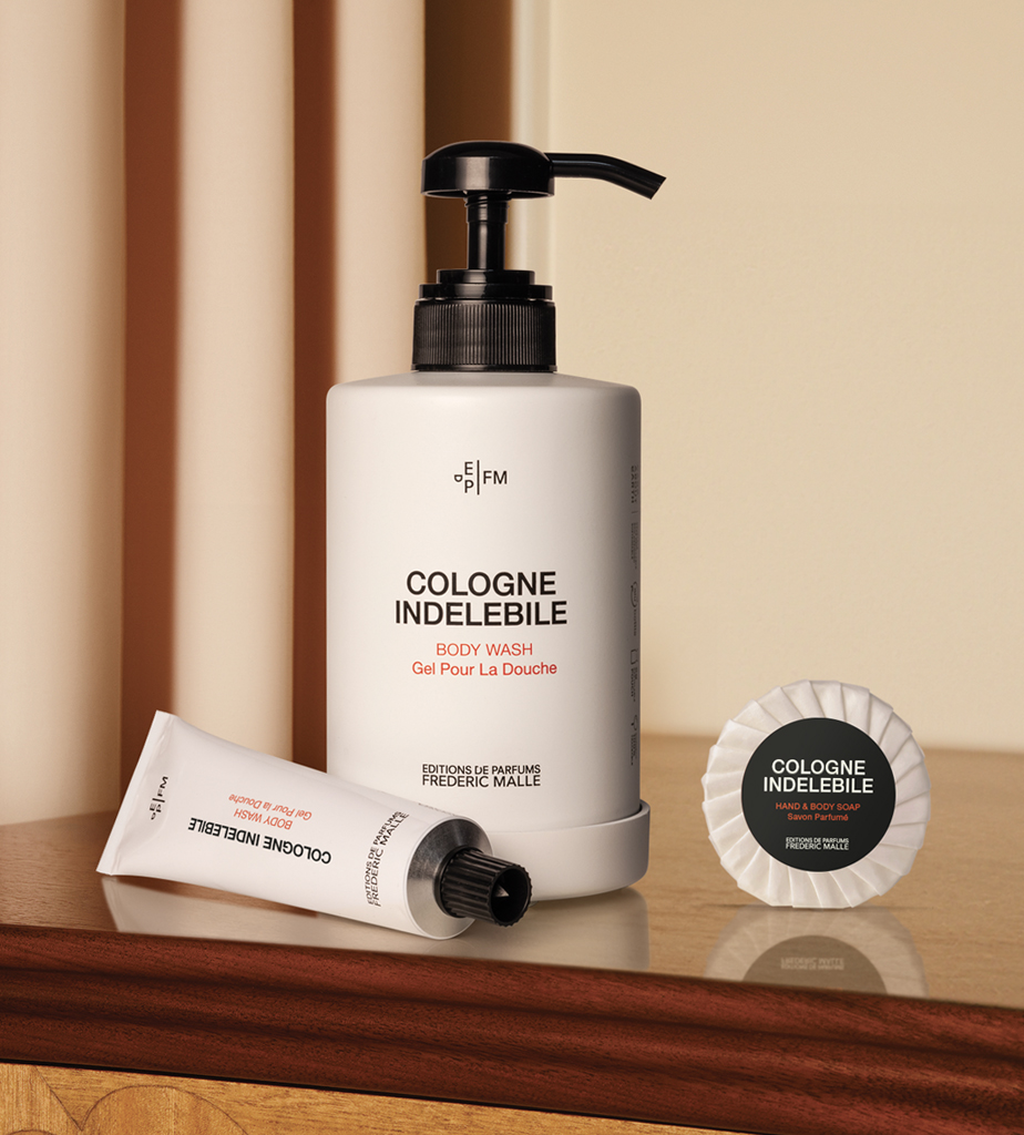 A bottle of body wash labeled "Cologne Indélébile" sits beside a tube and a circular compact, all set on a wooden surface.