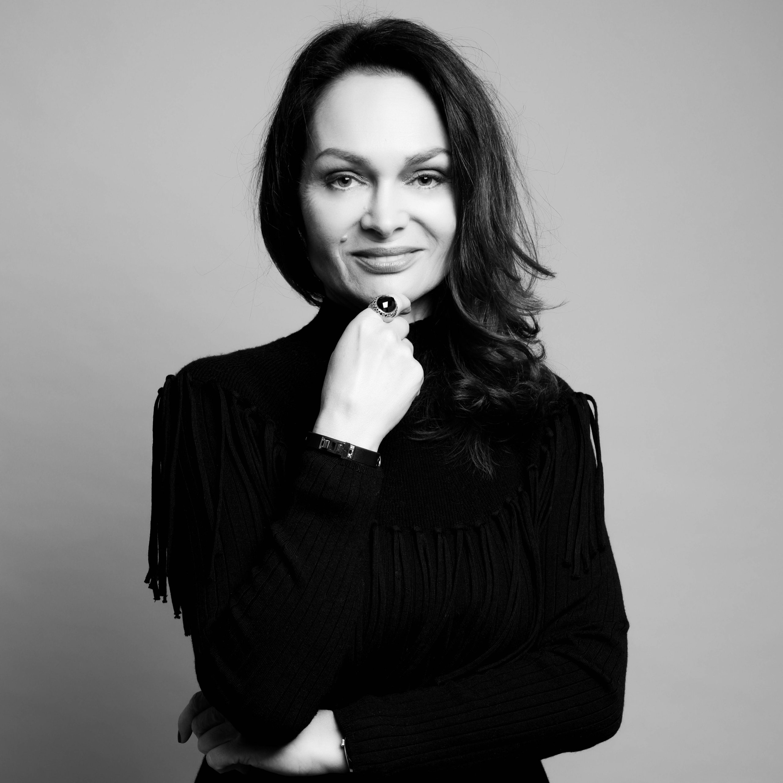 Black-and-white studio portrait of Chrystelle Lannoy wearing a dark high-neck sweater, posing with one hand under the chin against a plain gray background.