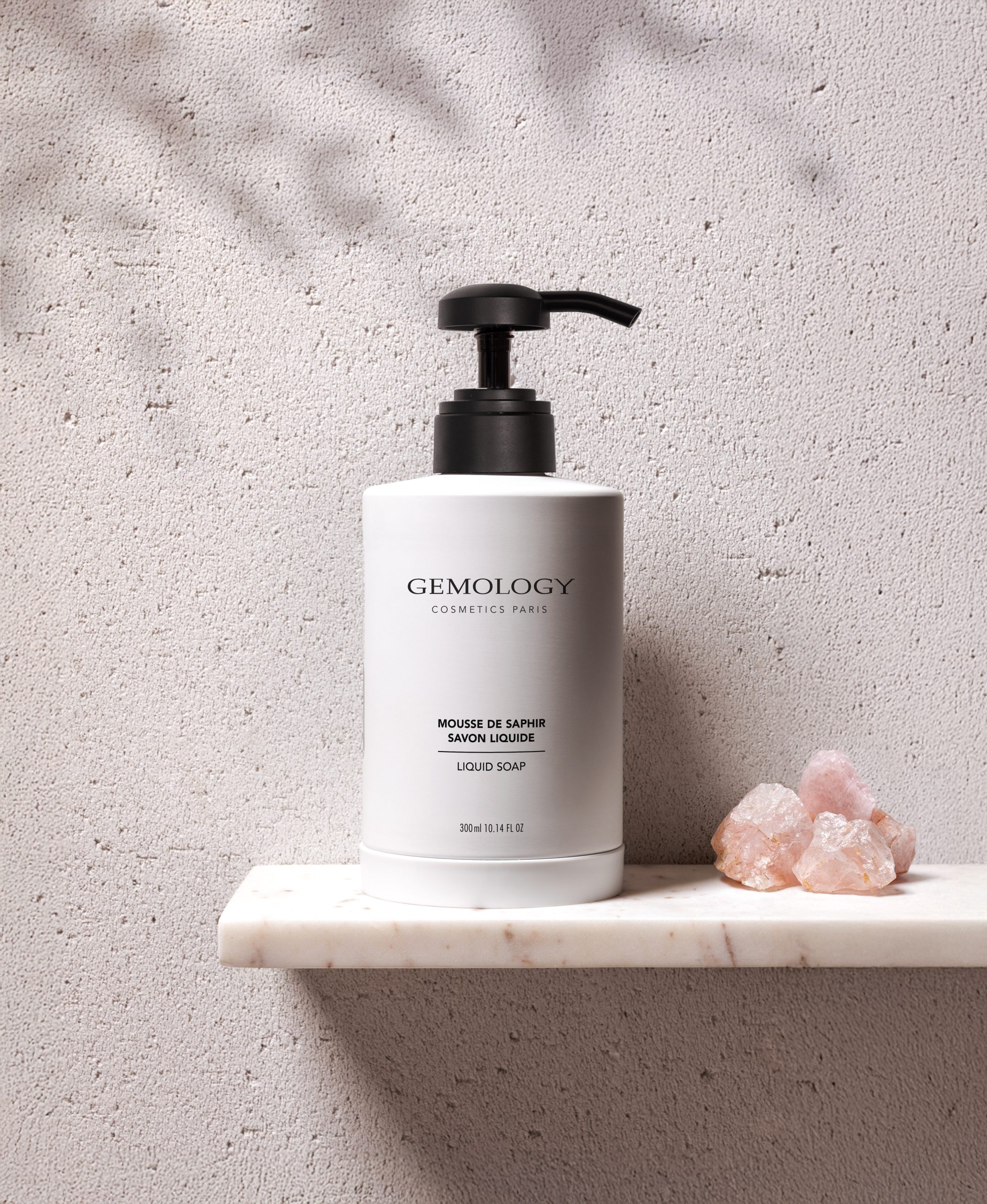 Gemology liquid soap bottle displayed on a marble shelf with rose quartz stones.