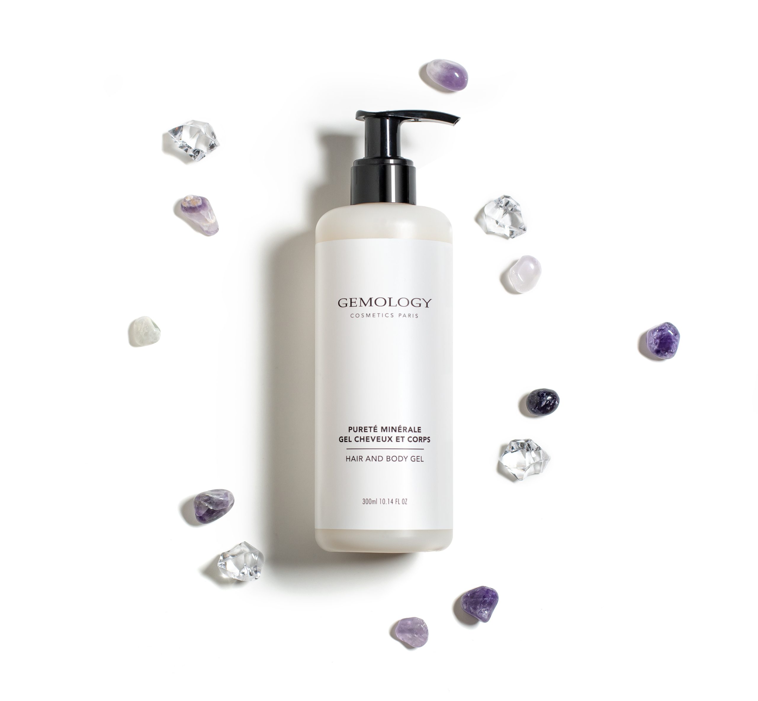 Gemology hair and body gel bottle surrounded by decorative gemstones on a white background.