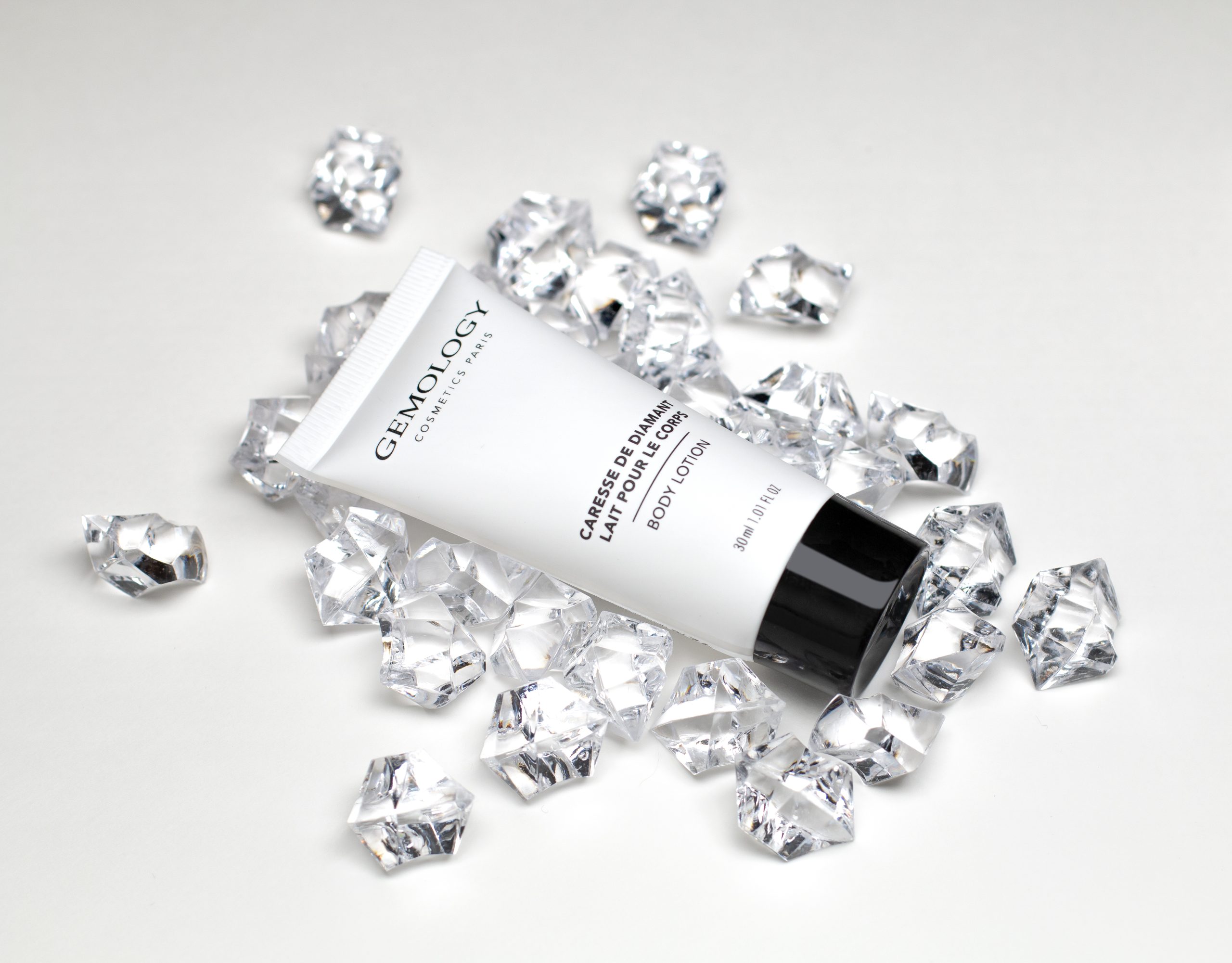 Gemology body lotion tube surrounded by crystal-inspired gemstones on a white background.