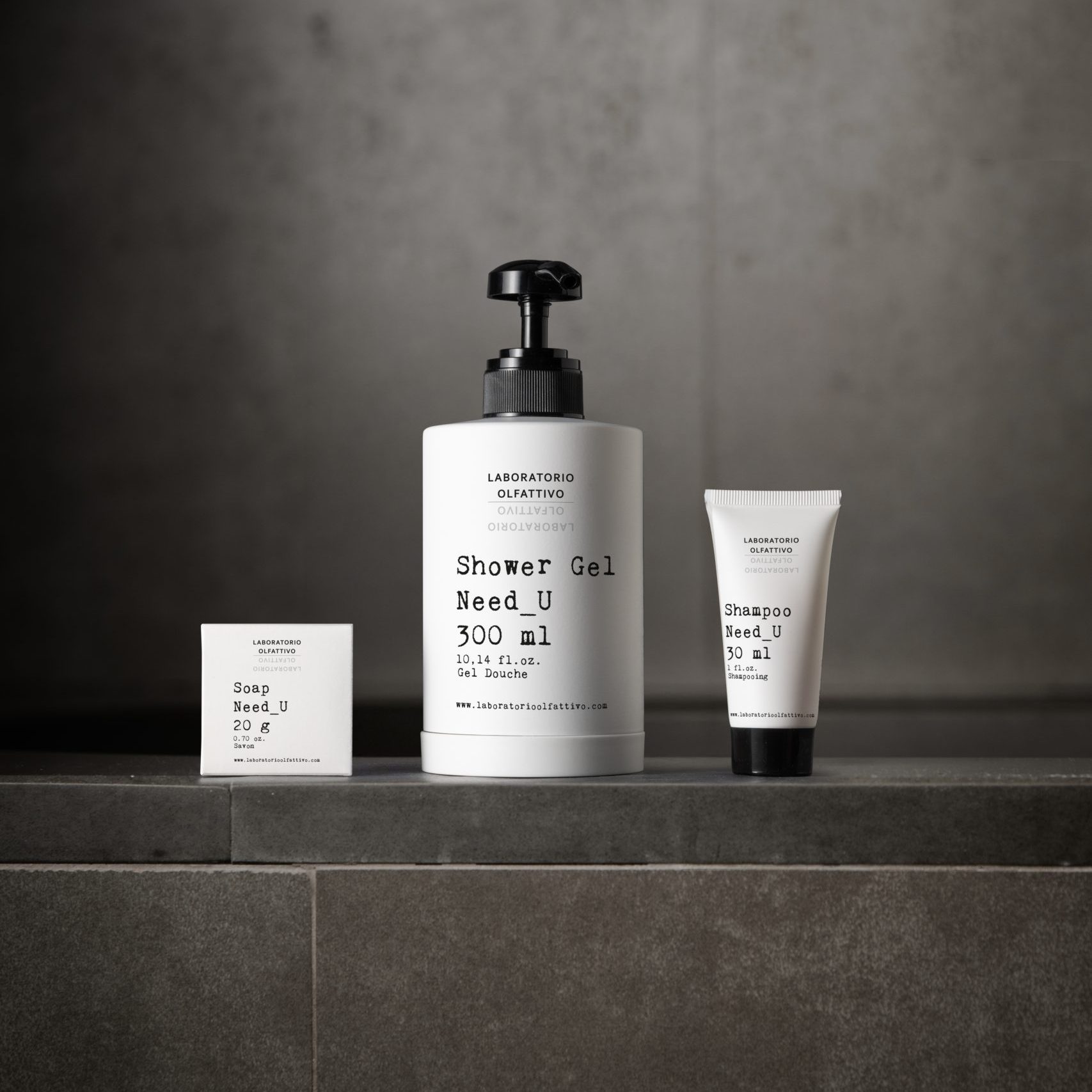 Laboratorio Olfattivo Need_U toiletries, including soap, shower gel, and shampoo, displayed on a dark stone bathroom shelf with a minimalist, contemporary aesthetic.