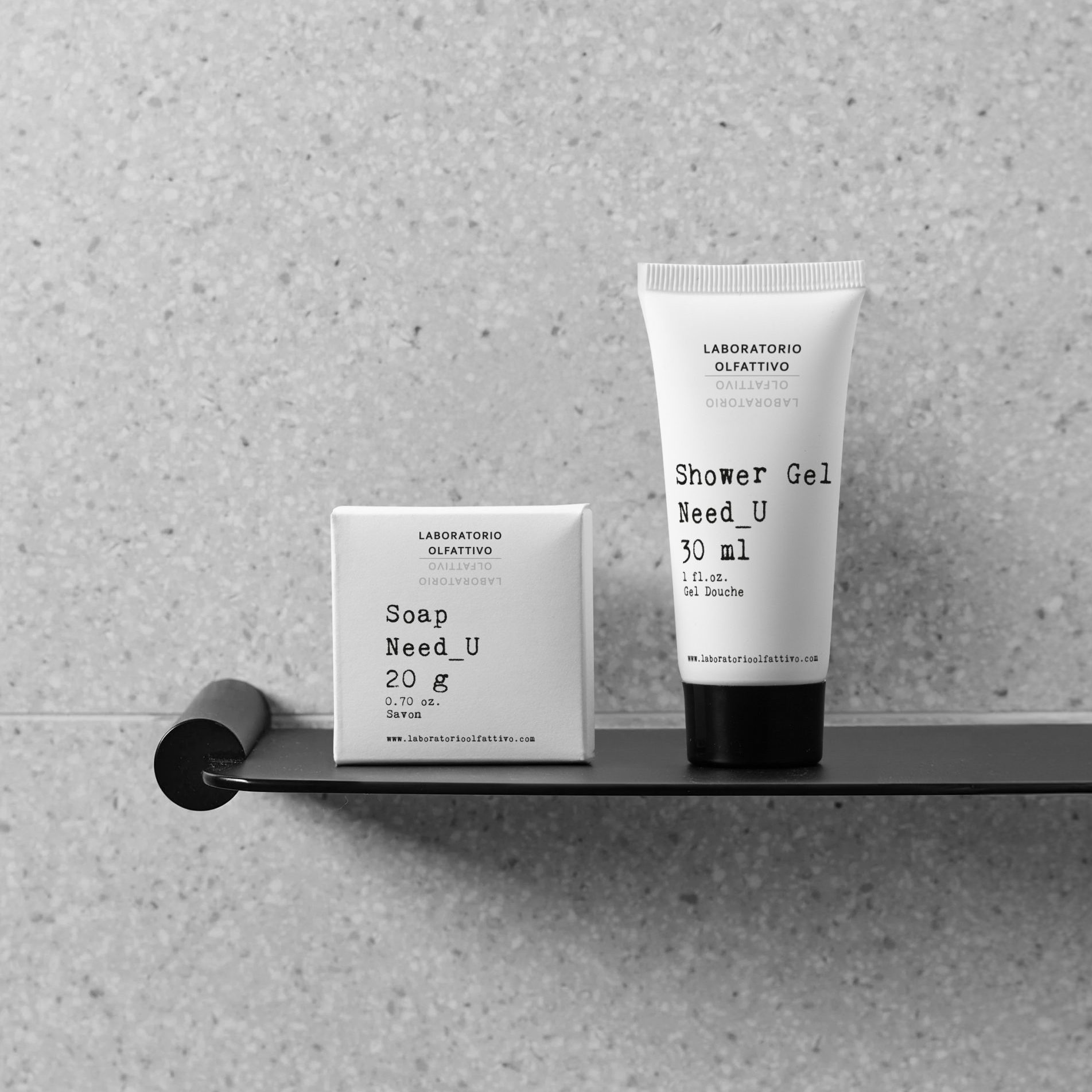 Laboratorio Olfattivo Need_U soap and shower gel displayed on a sleek black shelf against a light stone wall, showcasing a minimalist bathroom aesthetic.