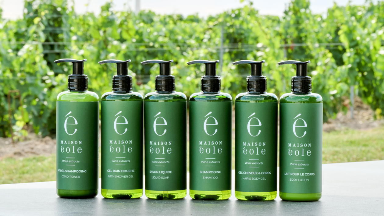 Maison &Eacute;ole wine-extract body care products displayed in front of a vineyard.